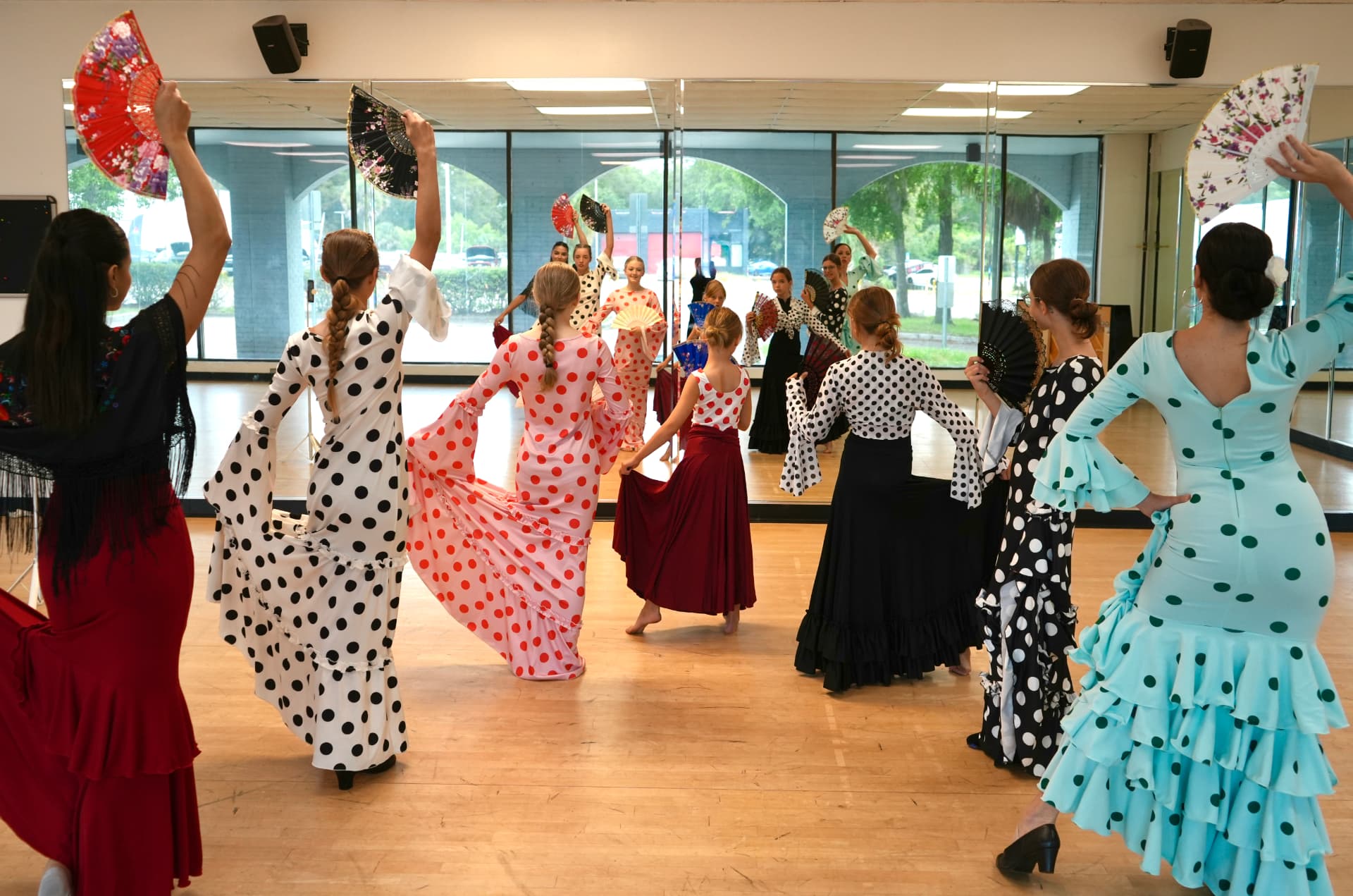 Flamenco students in polka-dot dresses dancing with fans in the studio